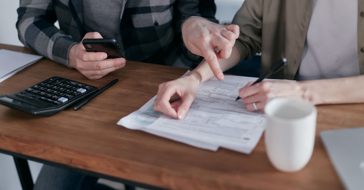 Compare Debt Solutions A couple analyzing financial documents and using a calculator at a home table.