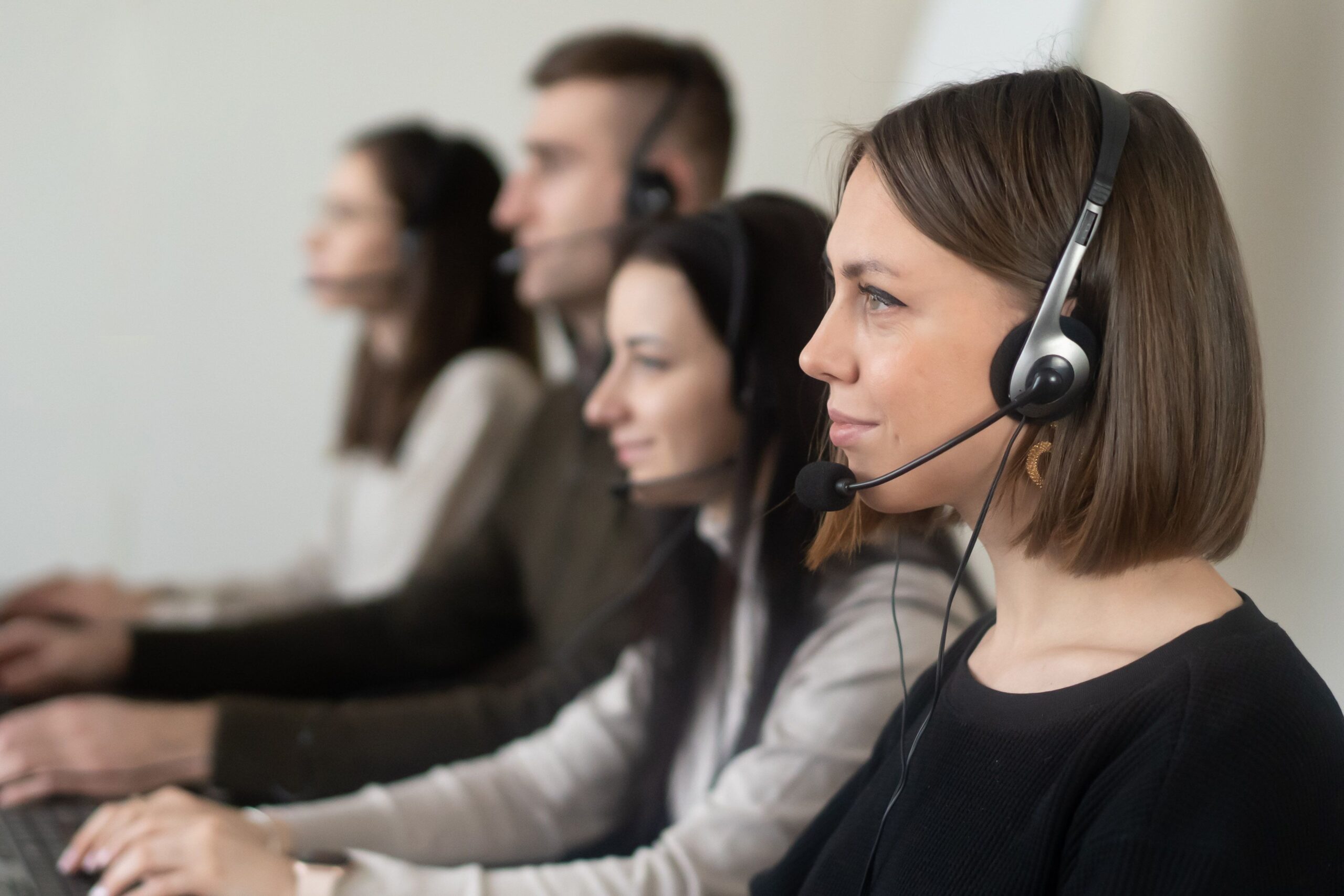 Compare Debt Solutions Side view of young coworkers in casual clothes sitting in light workplace with headphones with microphone while surfing on laptop