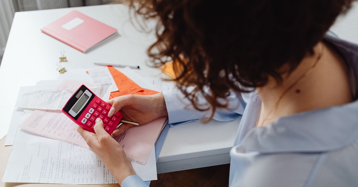 Compare Debt Solutions Woman calculating expenses with documents and calculator at work desk.