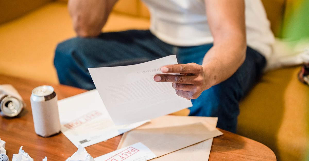 Compare Debt Solutions Man sitting on sofa reading unpaid bills, looking stressed and concerned over financial debt.